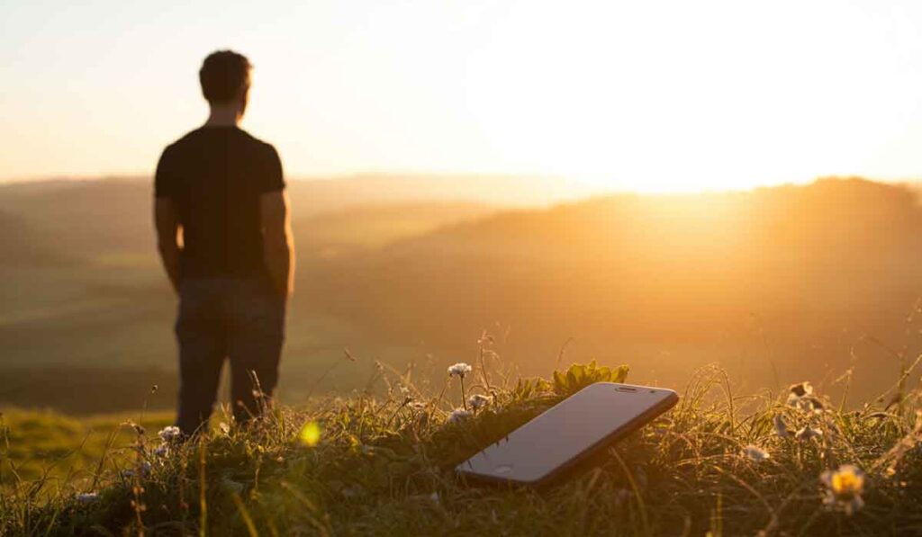 A man standing in the grass with a phone on the ground.