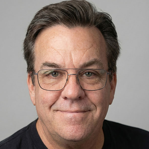 Middle-aged man with short brown hair, glasses, and a black shirt, smiling slightly at the camera against a plain gray background.